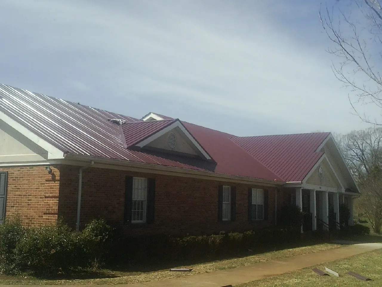 Red metal roof with gabled entries on a long brick building, from a Hail Damage Roof Repair job in Elsinore