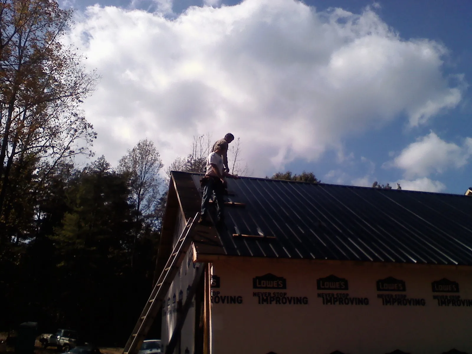 Roofer fastening dark metal panels high against a cloudy sky, from a Roof Inspection job in Elsinore