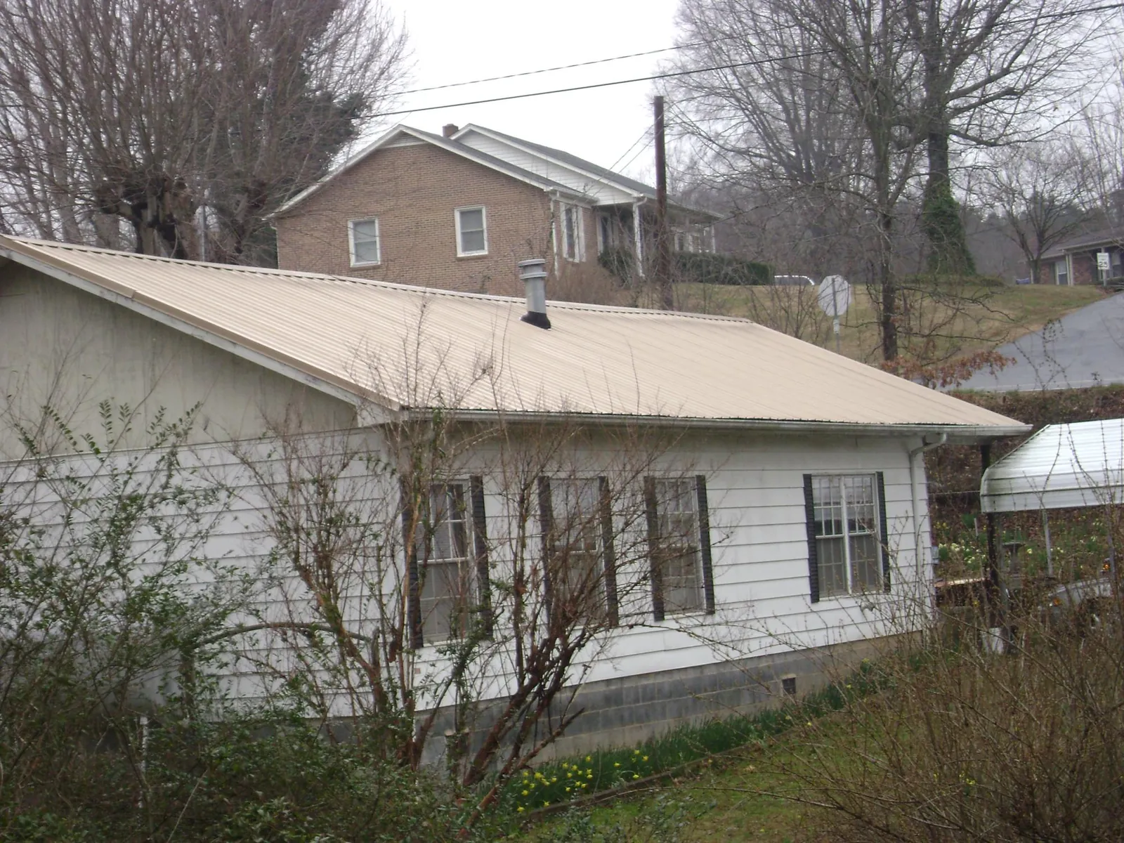 Tan metal roof on a white sided house set into a hillside — Commercial Roofing by Roofing Brothers in Elsinore